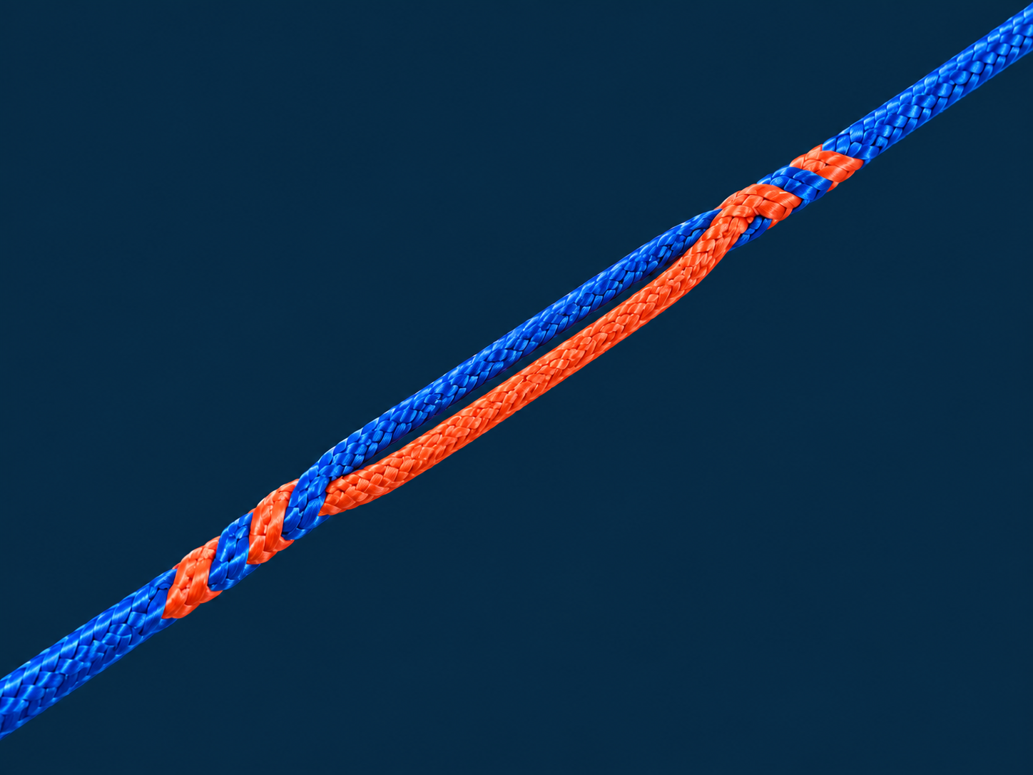 Studio close-up of one orange eye splice lying alongside continuous blue braided rope, with tapered woven joins at both ends, on a plain navy background.